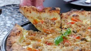 Fatia de pizza de caranguejo com tomate cereja e manjericão sendo servida