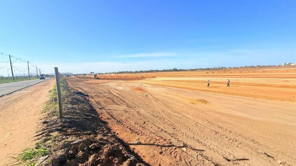 Terreno do condomínio de lotes na Serra após terraplanagem, às margens da Avenida Porto Dourado, com máquina e trabalhadores