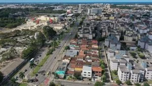 Vista aérea de bairro da Serra, cidade mais populosa do Espírito Santo, com avenida movimentada, prédios e mar ao fundo