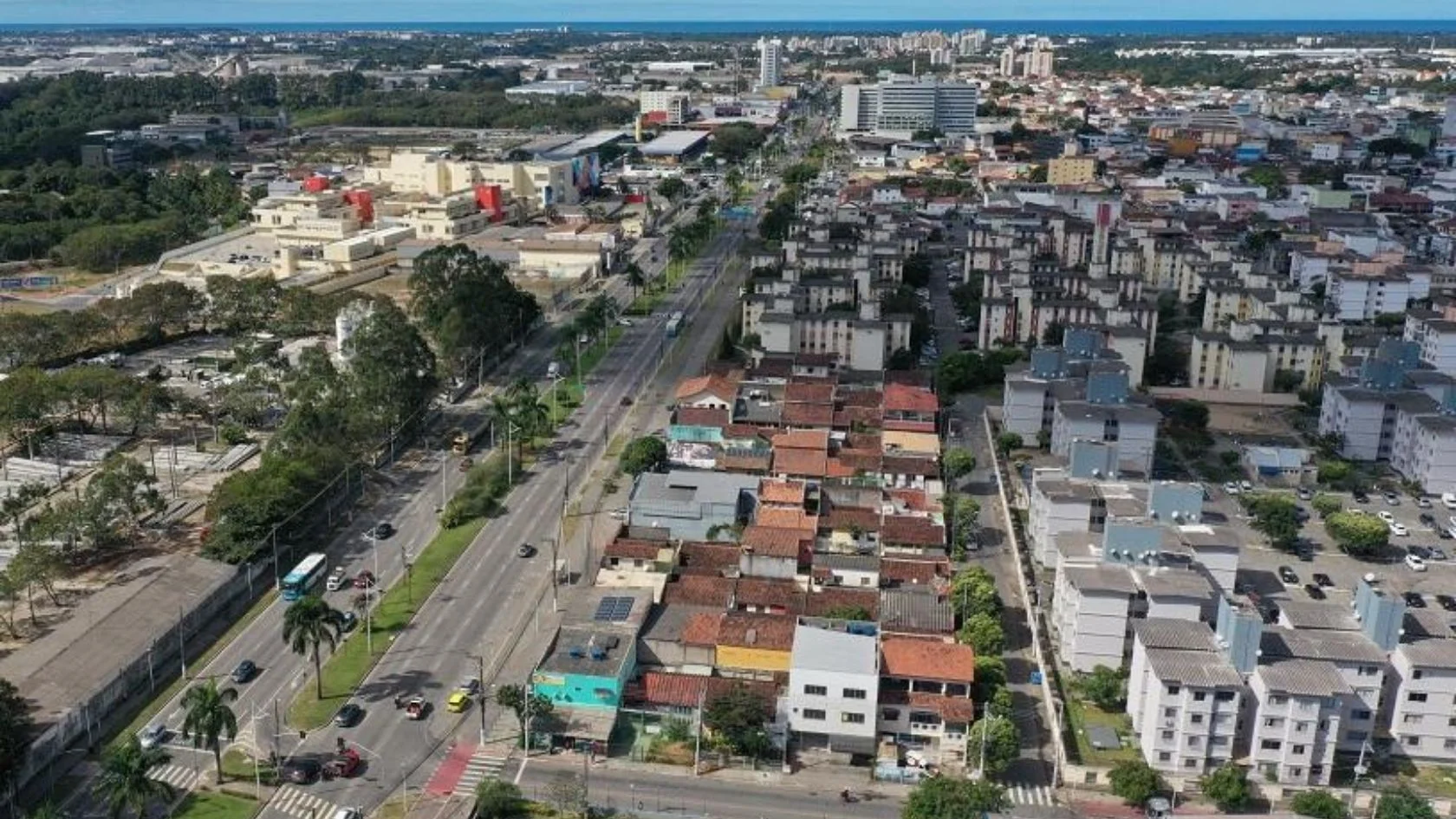 Vista aérea de bairro da Serra, cidade mais populosa do Espírito Santo, com avenida movimentada, prédios e mar ao fundo