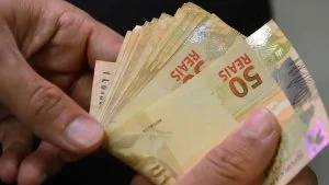 Mãos contam notas de 50 reais, referência ao pagamento do 13º salário 2026