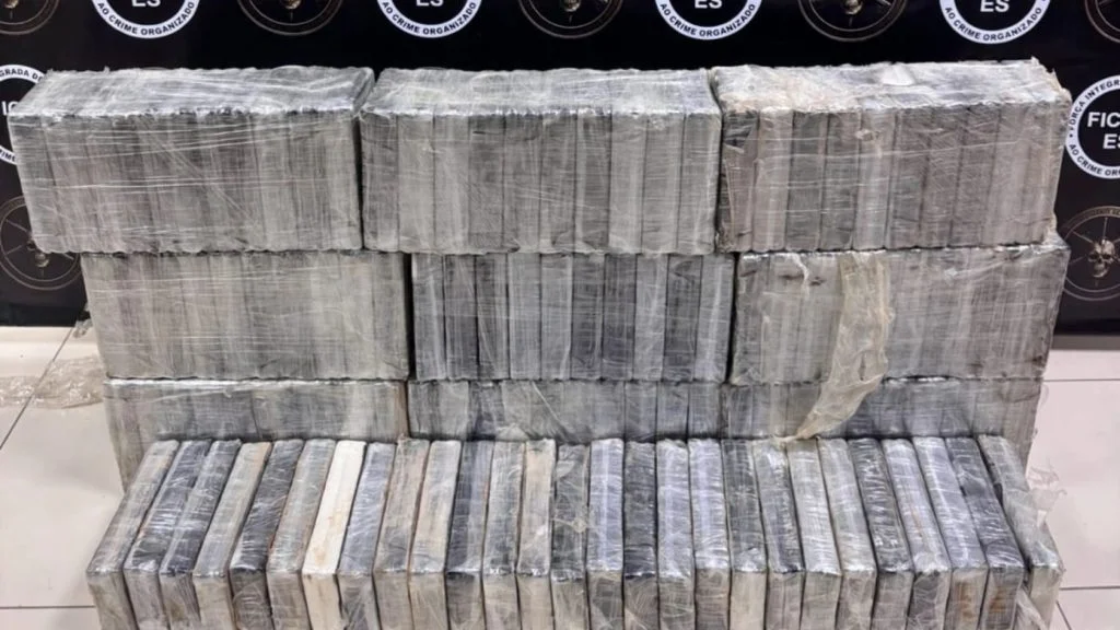 Tabletes de pasta base de cocaína apreendidos na Serra empilhados diante de painel da FICCO/ES