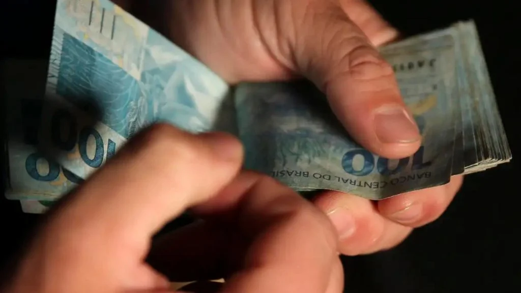 Mãos contam notas de R$ 100, ilustrando quanto ganhar para ser 1% mais rico no seu estado