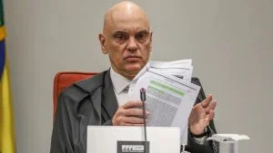 Alexandre de Moraes segura documentos durante sessão do STF, alvo de pedido de afastamento pela OAB-ES