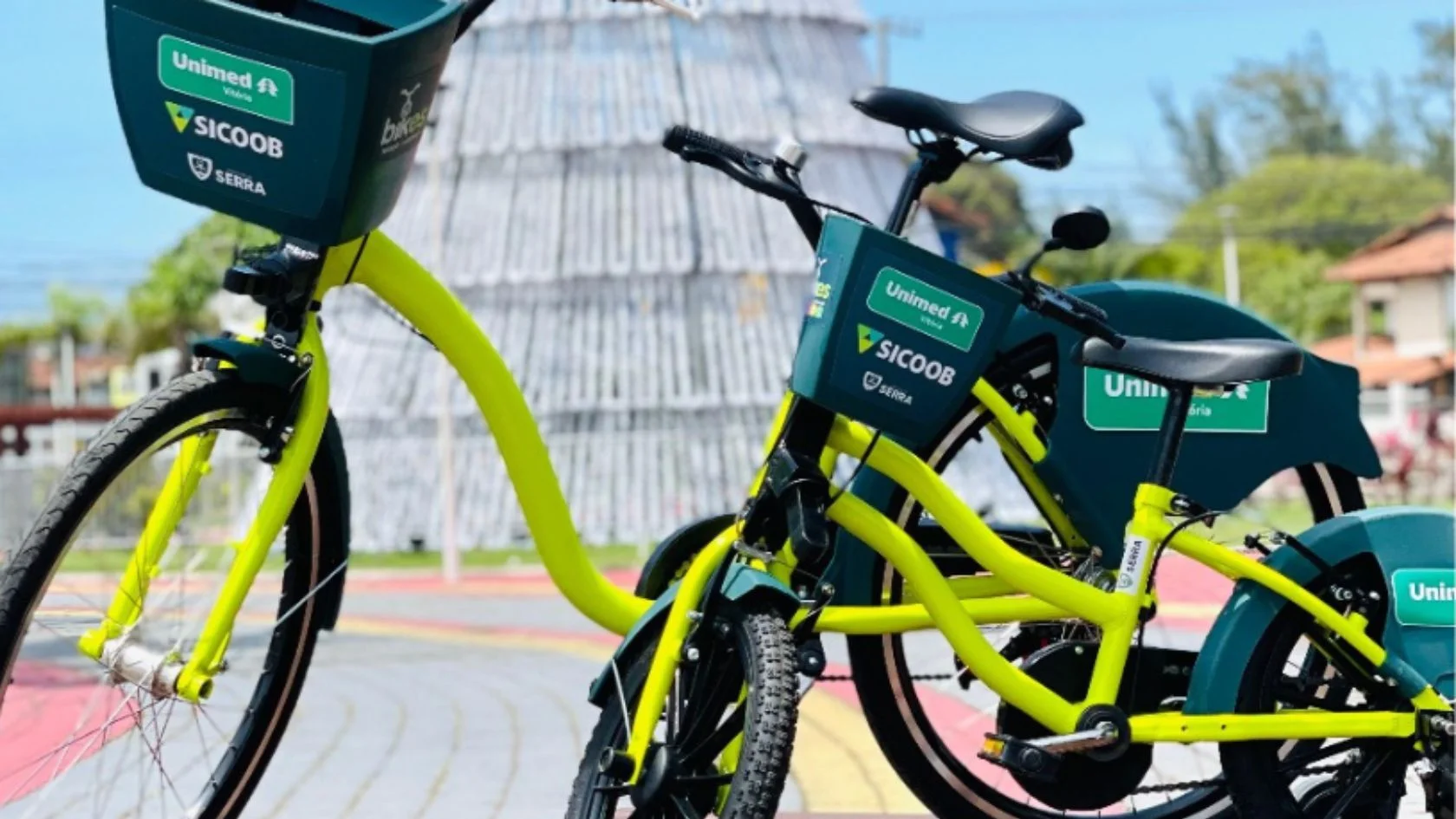 Bicicletas compartilhadas do BikES na Serra, amarelas com cestas verdes, lado a lado em calçada colorida