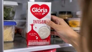 Mão segura caixa de leite UHT integral Glória de 1 litro na geladeira; lote do leite Glória foi interditado no RJ
