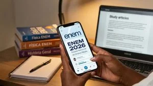 Local de prova do Enem 2026: estudante segura celular com tela do exame em mesa com livros e notebook