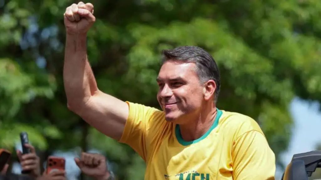 Flávio Bolsonaro de camisa amarela ergue o punho e sorri para apoiadores; candidato venceu a votação na Serra