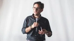 Fernando Cinelli, ex-presidente da Apex Partners, fala ao microfone de camisa xadrez e óculos