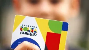 Criança segura cartão do Bolsa Família em primeiro plano; pagamento de outubro chega com reajuste