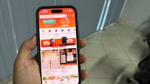 Mão segura celular com a tela inicial do app da Shopee, onde ficam as moedas usadas na promoção da Shopee