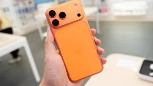 Mão segura iPhone da linha 17 Pro na cor laranja; modelos estão no leilão da Receita Federal