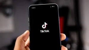 Mão segura celular com o logotipo do TikTok na tela; app entra no debate sobre redes sociais para menores de 16 anos