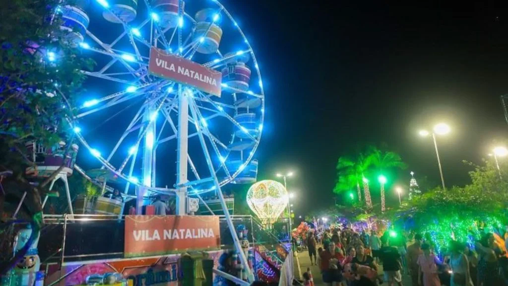 Roda-gigante iluminada de azul na vila natalina, com público circulando entre luzes de Natal na Serra em edição anterior
