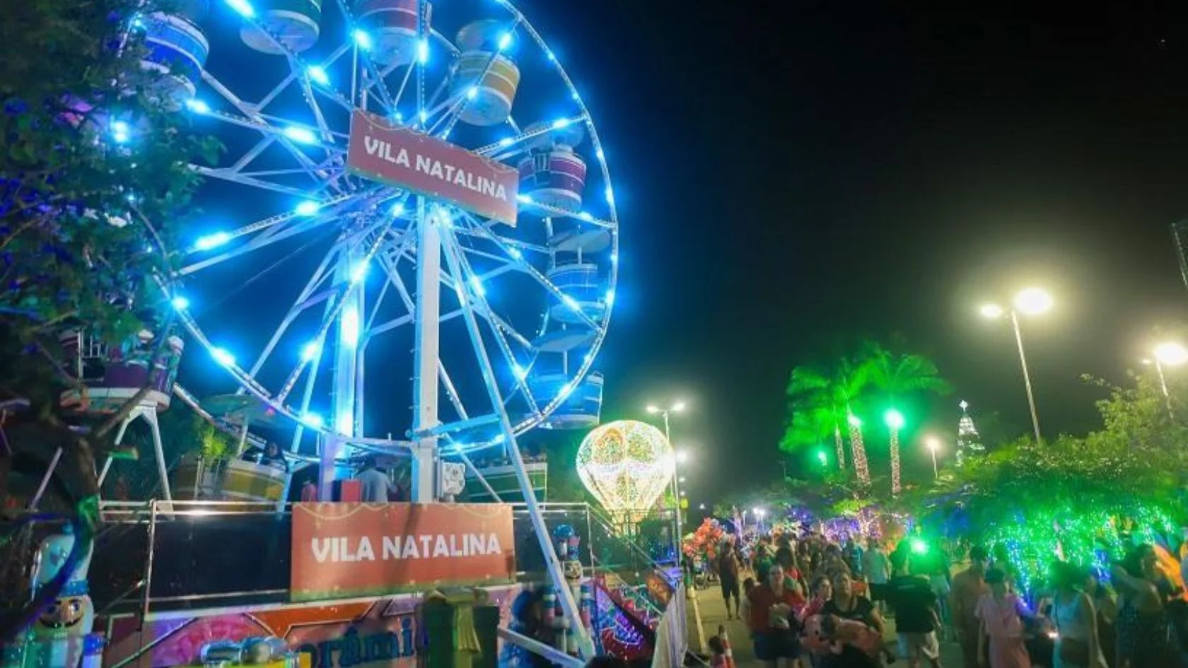Roda-gigante iluminada de azul na vila natalina, com público circulando entre luzes de Natal na Serra em edição anterior