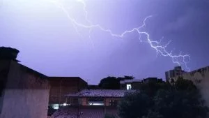 Raio corta o céu sobre telhados e prédios em noite de tempestade, ilustrando alerta de tempestade na Grande Vitória