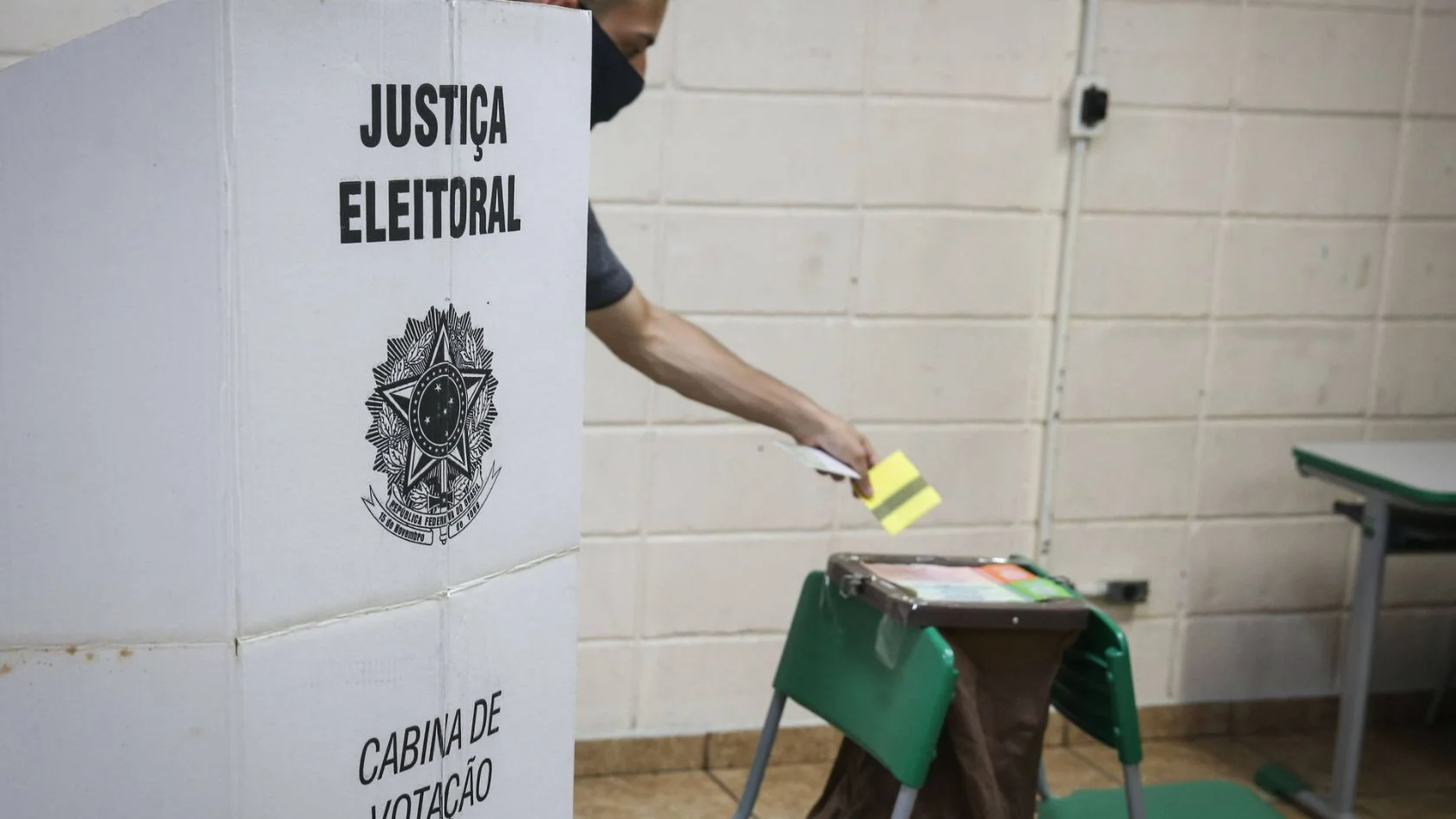Eleitor de máscara ao lado da cabine de votação da Justiça Eleitoral, em imagem de arquivo sobre a votação prorrogada