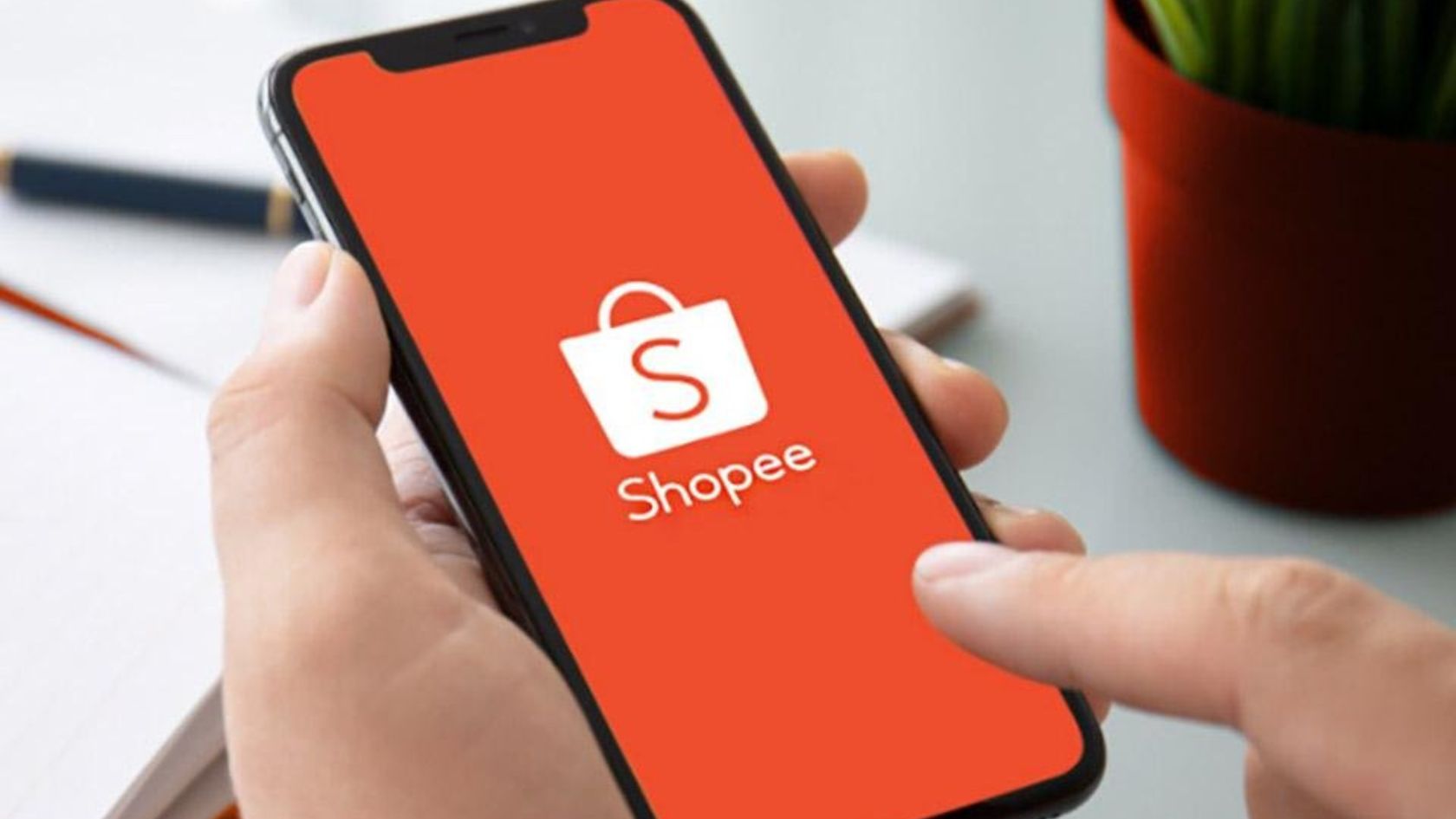 Mão segura celular com o logotipo da Shopee na tela, plataforma que libera cupons do 11.11