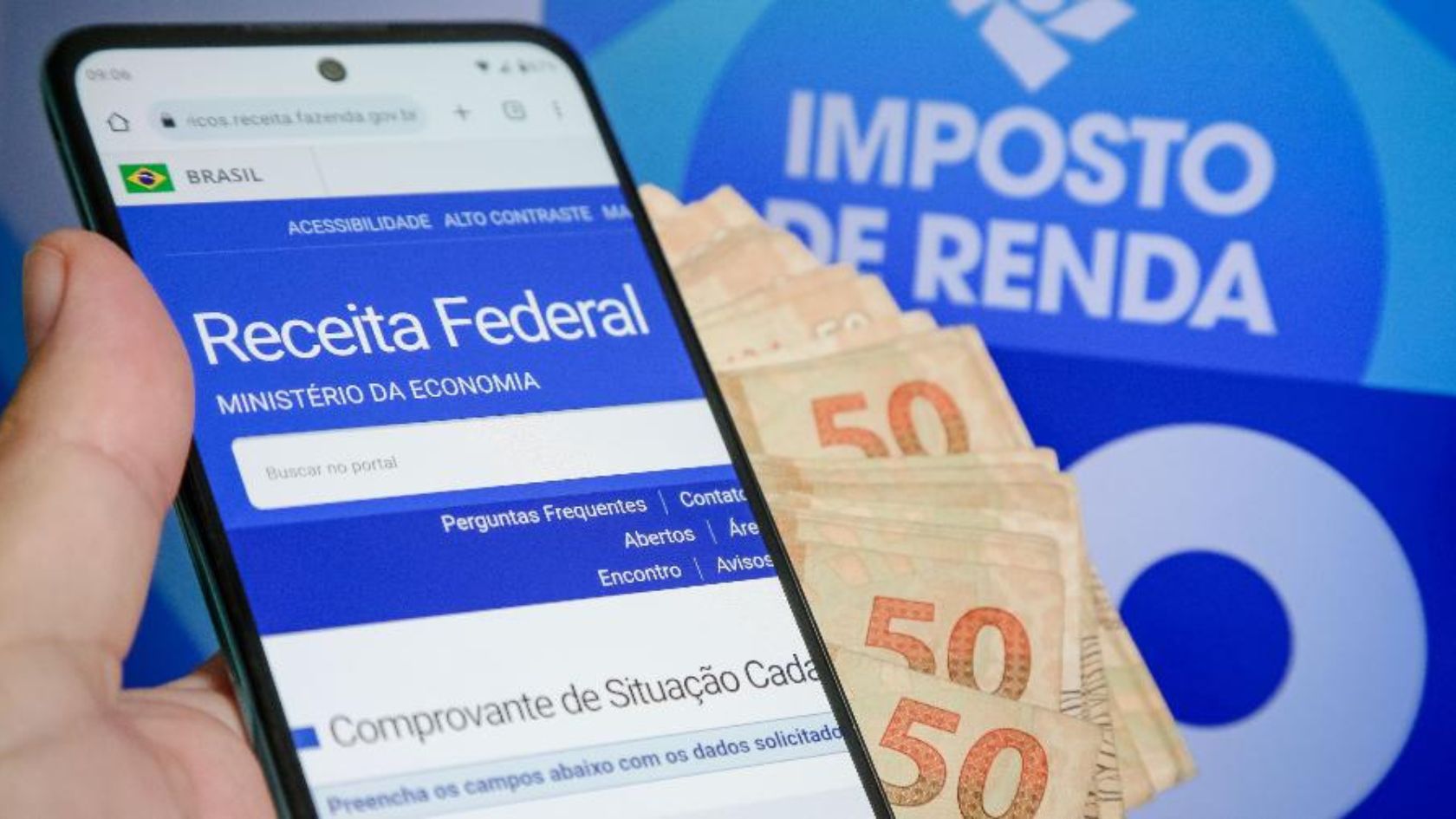 Mão segura celular com site da Receita Federal ao lado de notas de R$ 50; imagem ilustra lote residual de restituição