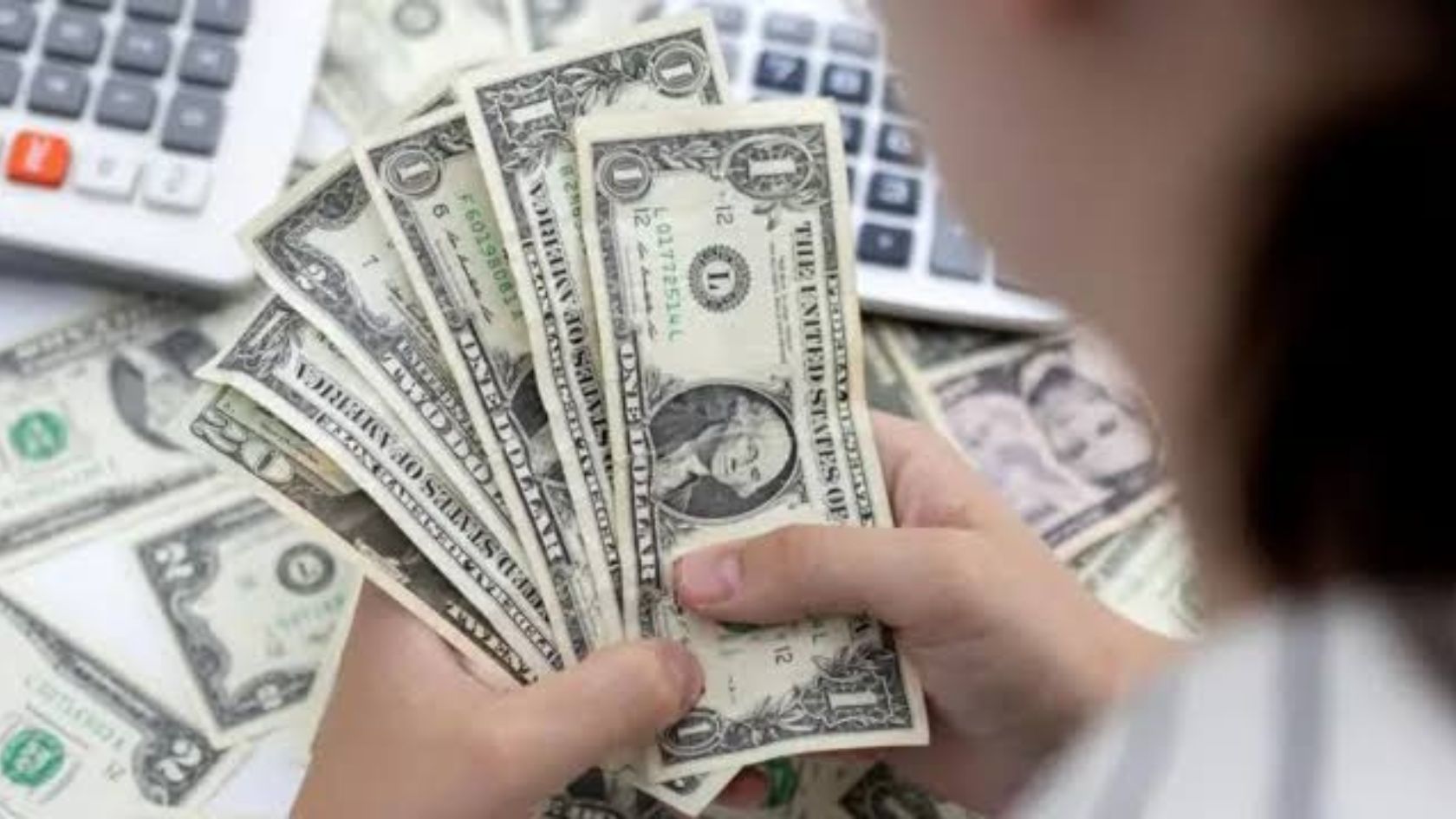 Mãos seguram notas de dólar sobre mesa com calculadoras, em imagem ilustrativa da alta do dólar