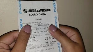 Mãos seguram recibo de bolão da Mega da Virada da Caixa; apostas da Mega da Virada 2026 começam em 3 de novembro