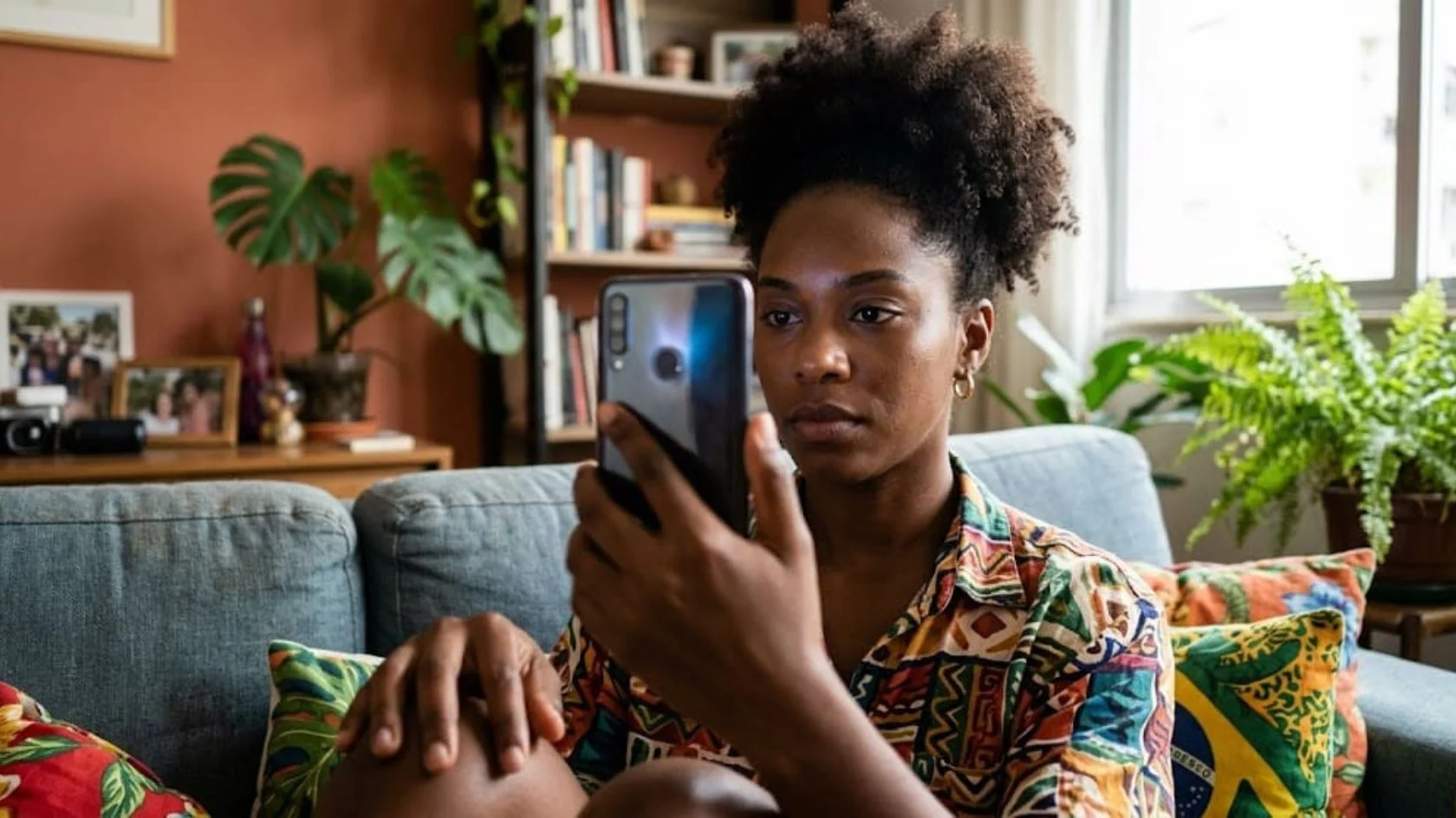 Mulher sentada no sofá aponta o celular para o rosto, gesto usado na biometria da Anatel por reconhecimento facial