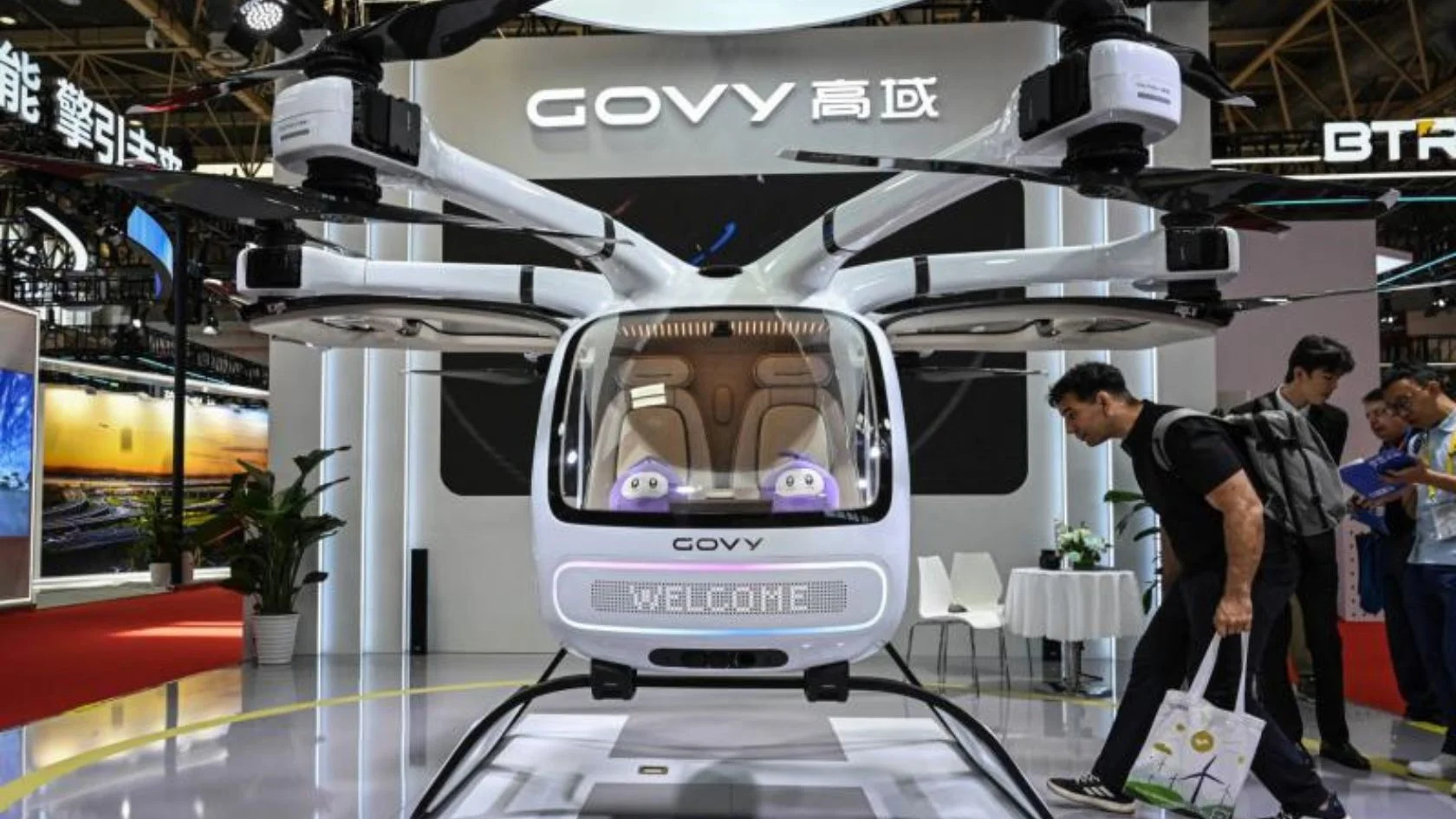 Carro voador da GAC, o Govy AirCab, exposto em feira com visitantes olhando a cabine de dois lugares