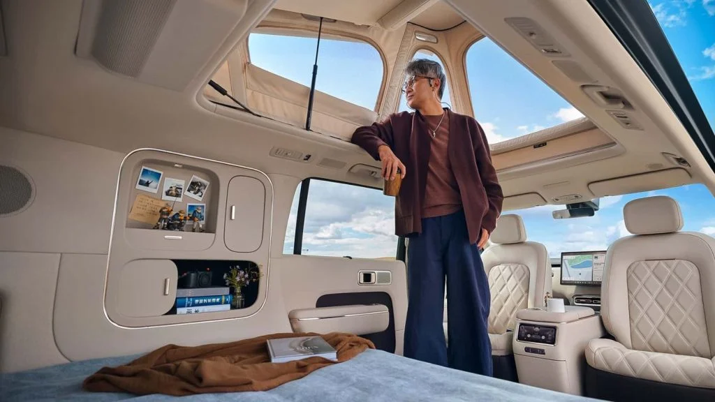 Homem observa a paisagem de dentro do carro da Xiaomi com teto elevado, cama e bancos de couro bege