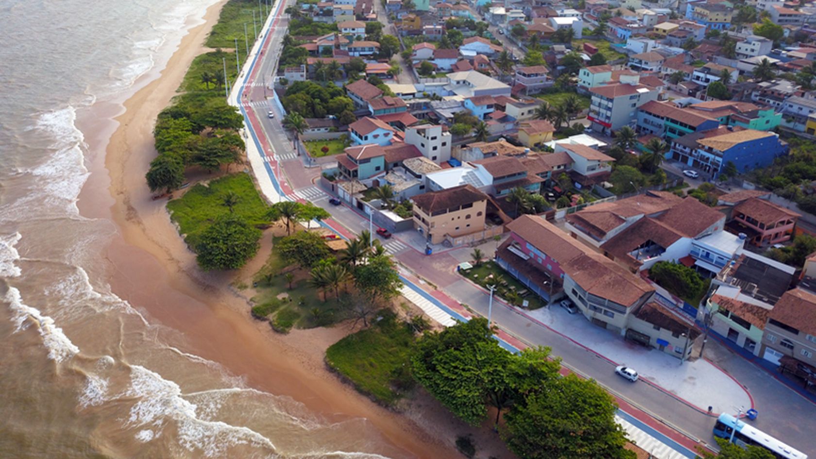Vista aérea da orla com avenida, ciclovia e casas à beira-mar, em região de imóveis no litoral da Serra