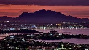 Vista aérea ao anoitecer, com baía, ilhas, prédios iluminados e serra ao fundo, ilustra matéria sobre preço do apartamento na Serra