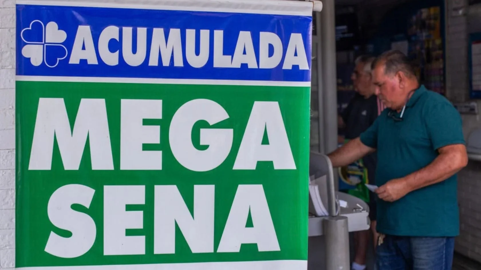 Faixa de Mega-Sena acumulada na entrada de lotérica, com apostador segurando volante no balcão de apostas ao fundo