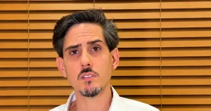 Fernando Cinelli, ex-presidente da Apex, fala à câmera de camisa branca, diante de persiana de madeira